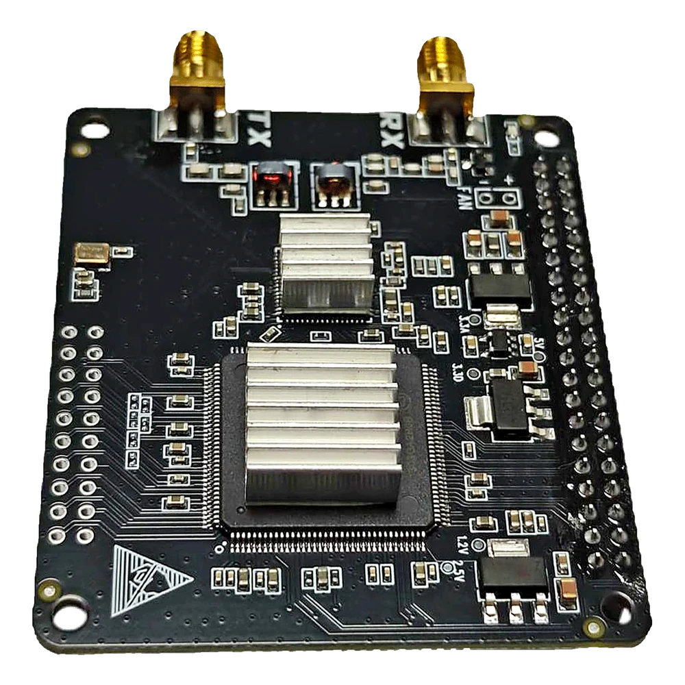 The RadioBerry V2 HAT seen at an angle: a black square circuit board with two gold SMA connectors marked TX and RX along the top edge, two finned aluminium heatsinks over the FPGA and the transceiver chip, and the Raspberry Pi header along the right-hand edge.
